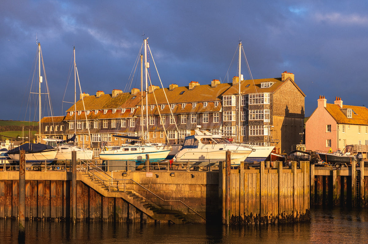 Golden evening light on the harbour boats and buildings at West Bay, Dorset