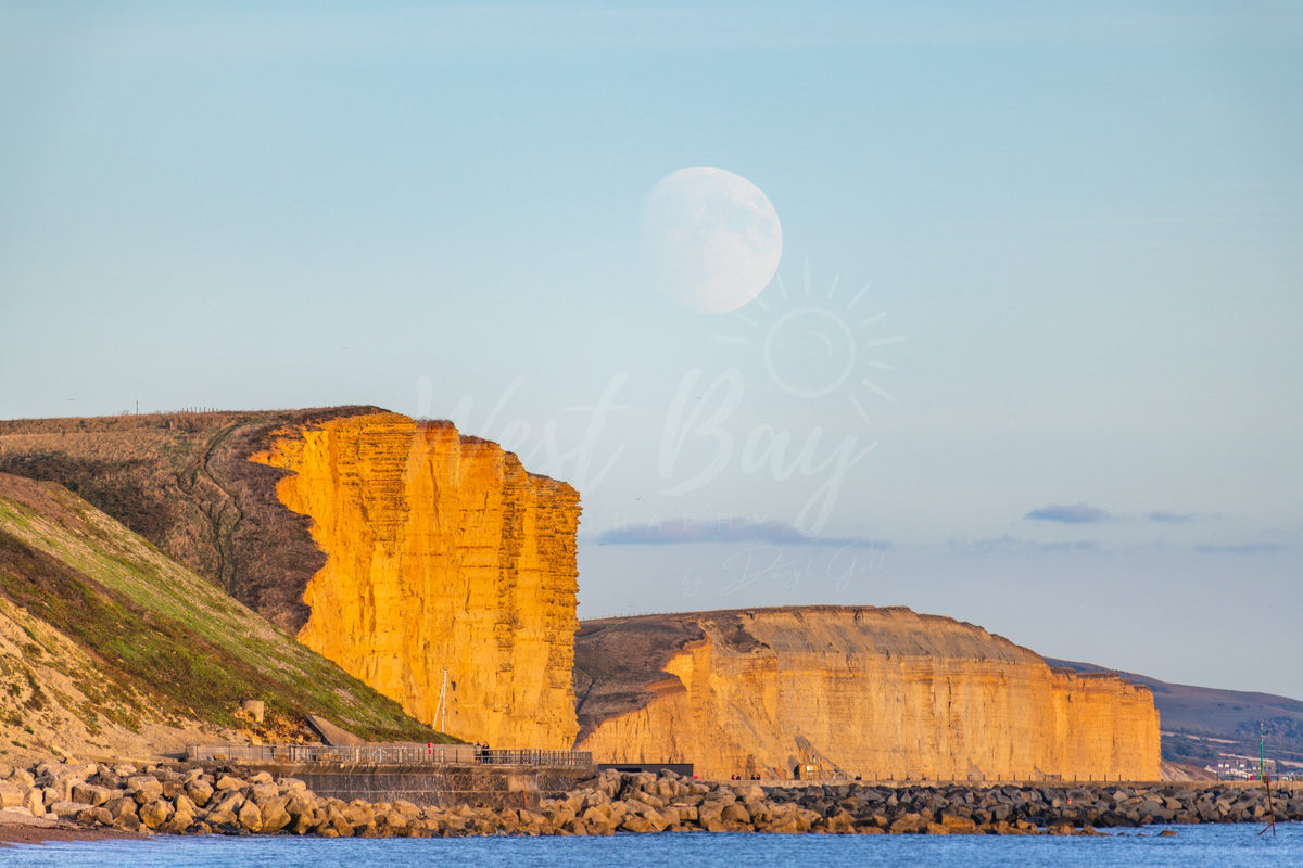 Landscape photograph of the moon above sunlit East Cliff, photographed from Eype Beach near West Bay, Dorset