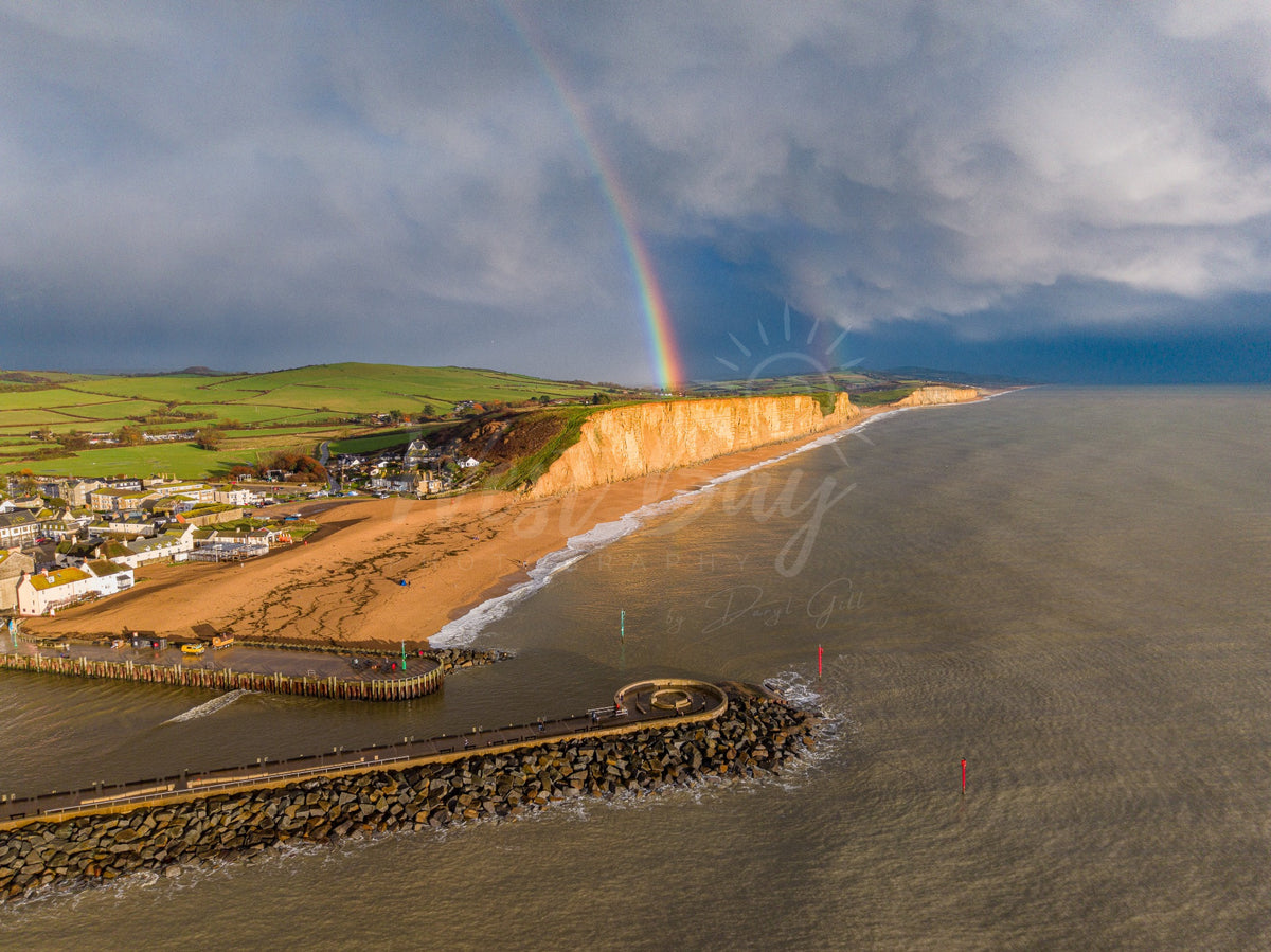 Landscape aerial view of a rainbow over East Cliff, with West Bay harbour and both piers in the foreground