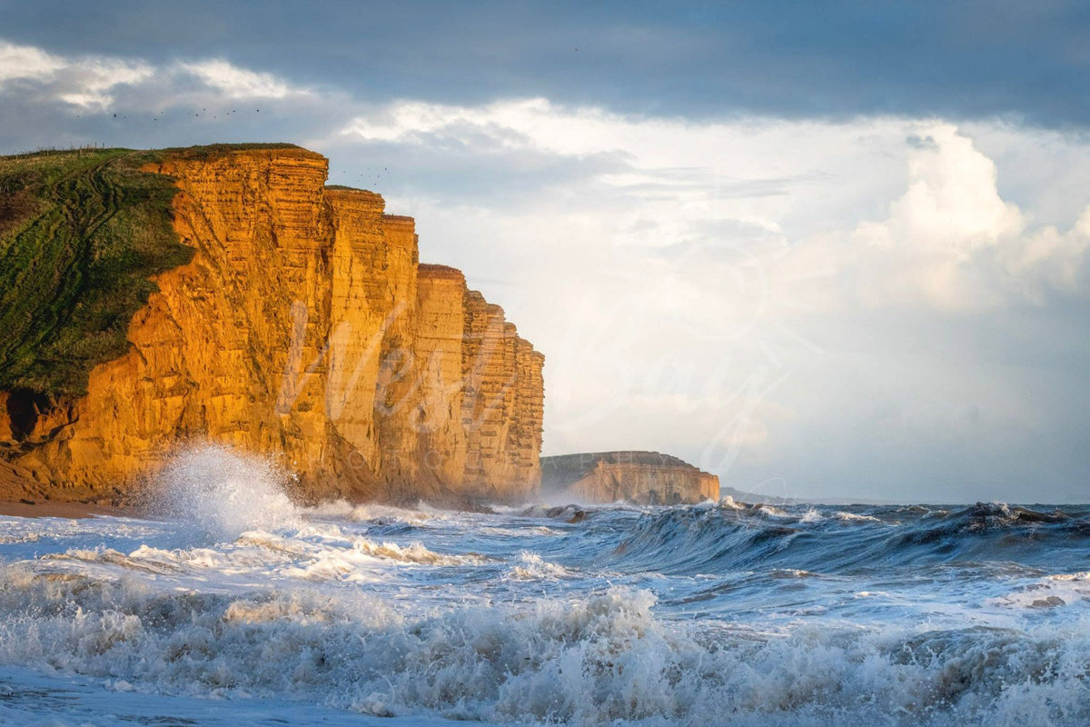 Golden sunlight on East Cliff with rough seas at West Bay, Dorset